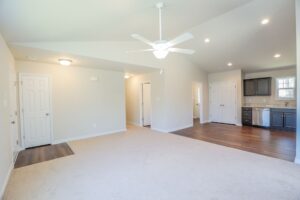 Open living area with beige carpet, ceiling fan, and kitchen—ideal for new homes in Richmond VA.