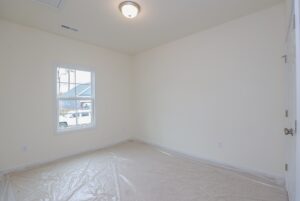 Empty room in new homes in Richmond VA with white walls, ceiling light, window, and plastic on carpeted floor.