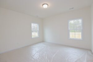 Empty, unfurnished room in one of the new homes in Richmond VA; cream walls, two windows, and carpet covered in plastic.