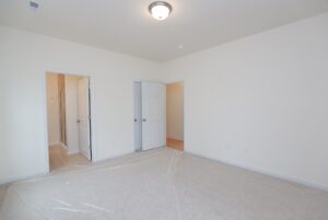 Empty bedroom in one of the new homes in Richmond VA; beige carpet, white walls, two open doors, floor covered in plastic.