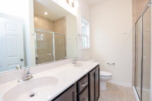 Modern bathroom in new homes in Richmond VA features a double sink vanity, large mirror, glass shower, and neutral tile.
