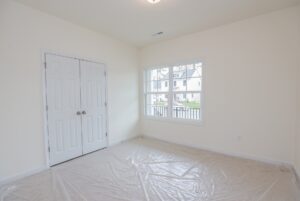 Empty room in one of the new homes in Richmond VA with light walls, double closets, large window, and plastic sheeting on floor.