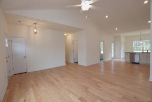 Spacious open-plan room in new homes in Richmond VA, with light wood floors, white walls, and ceiling fans leading to kitchen.
