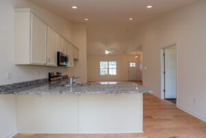 Modern kitchen with granite countertops, wood floors, and open living area in new homes in Richmond VA.