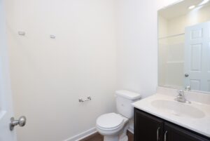 A clean, minimal bathroom perfect for new homes in Richmond VA, featuring a toilet, sink, and mirror on a white wall.