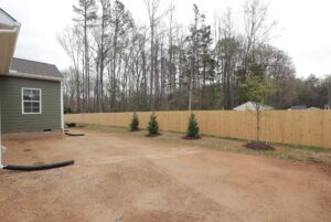 A fenced backyard with young trees and bare dirt, perfect for new homes in Richmond VA next to a green house.