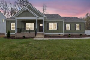 Green single-story house with front porch, lights on at dusk—a charming glimpse of new homes in Richmond VA.