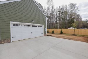 Green house exterior with white double garage, driveway, and yard—perfect for new homes in Richmond VA.