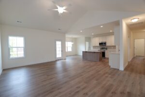 Spacious open-plan living in new homes in Richmond VA, with wood floors, ceiling fan, and a modern kitchen with white cabinets.