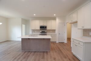 Modern kitchen in new homes in Richmond VA, featuring white cabinets, an island, stainless appliances, and wood-look flooring.