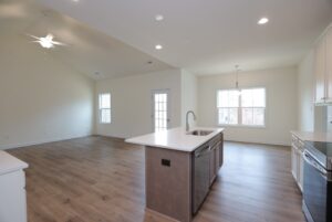 Open, empty kitchen and living area with wood floors in new homes in Richmond VA; features large windows and an island sink.