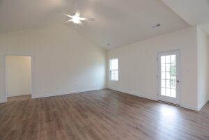 Bright empty room in new homes in Richmond VA with wood floors, cream walls, ceiling fan, window, and glass door.