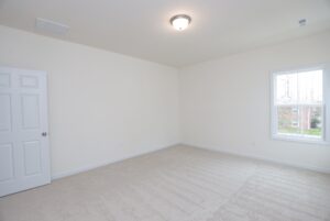 Empty, carpeted room in one of the new homes in Virginia with white walls, a closed door, ceiling light, and bright window.