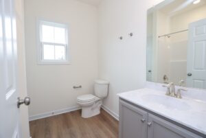 A simple bathroom in new homes in Richmond VA with a toilet, sink, mirror, and wood-look flooring.