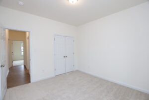 Empty room with beige carpet and double closets in one of the new homes in Richmond VA, featuring an open hallway access.