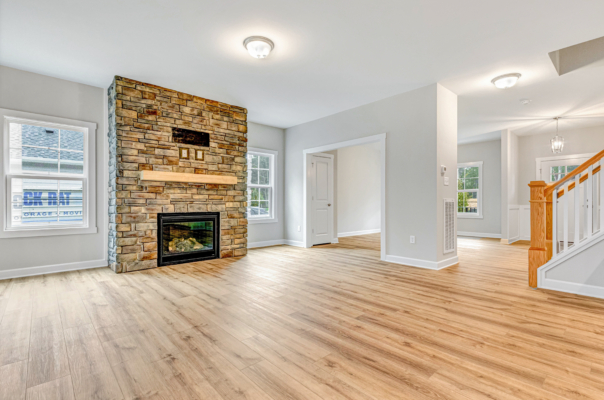 Spacious living room with stone fireplace, wooden floors, and large windows in a bright, modern new home.