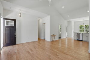 Bright, modern open-concept living area with light wood floors and white walls, leading to kitchen.