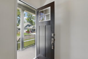 A dark wooden front door is open, revealing Poplar Village’s porch and Charles’ suburban neighborhood beyond.