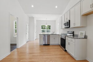 Modern kitchen at The Charles with white cabinets, stainless appliances, and light wood flooring, plus large windows.