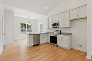 Modern kitchen with white cabinets, stainless steel appliances, and light wood flooring.