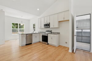 Modern kitchen at The Charles with white cabinets, stainless steel appliances, wood floors, and garage access.