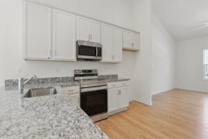 Modern kitchen with white cabinets and granite countertops in Poplar Village; open to empty living area.