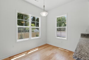 Bright, empty room with hardwood floors at The Charles, featuring large windows, white walls, and a hanging light fixture.