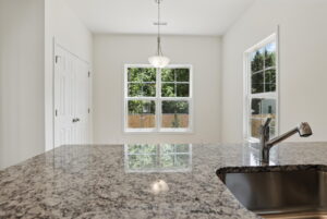 Granite kitchen countertop with sink, large windows, and hanging light at The Charles in a bright room.