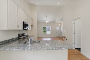 Modern kitchen with granite counters opens to a bright living area in Poplar Village with wood floors and ceiling fan.