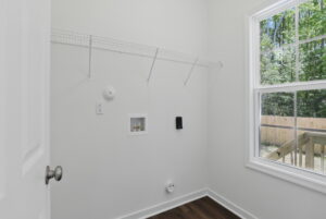 Empty laundry room with a wire shelf, hookups for washer and dryer, and a window showing a fenced yard.