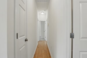 A narrow hallway in Poplar Village with white walls, wooden floor, and several closed doors on each side.