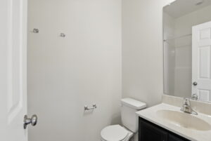 Minimalist bathroom at The Charles with white walls, toilet, sink, and towel rack on an empty wall.