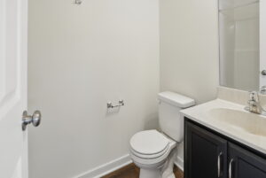Small bathroom with a white toilet, empty toilet paper holder, and a dark vanity with sink and faucet.