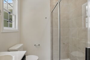 Modern bathroom at The Charles with glass shower, beige tile, white toilet, and natural light in Poplar Village.