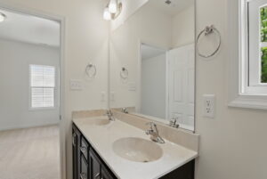 Bathroom with double sink vanity, large mirror, and view into an adjacent carpeted bedroom.