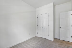 Empty room with white walls, beige carpet, a closed double closet, and an open door.