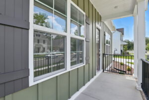 Green house front porch with windows and black railing in Poplar Village, overlooking The Charles and suburban homes.