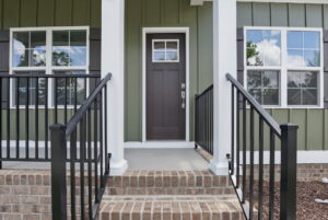 Front porch of The Charles in Poplar Village with brick steps, black railings, and a brown door with side windows.