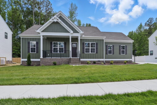 Single-story Poplar Village green house with white trim, front porch, and manicured lawn on a sunny day.