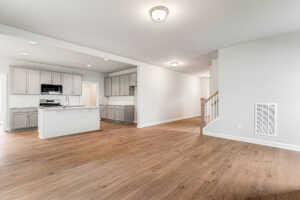 Empty modern kitchen and living area at Somerset Hill, with wood floors, light gray cabinets, and staircase on the right.