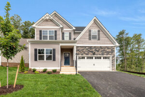 Two-story Somerset Hill home with gray siding, stone accents, two-car garage, and lush grass surrounded by trees.