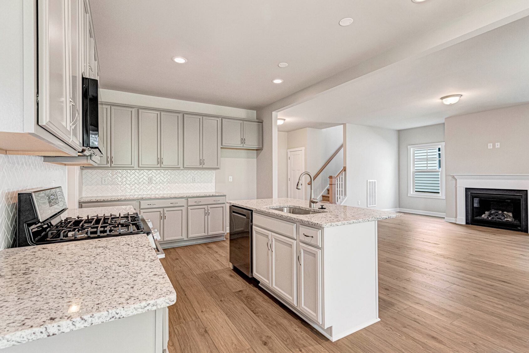 Modern Somerset Hill kitchen with white cabinets, granite counters, island sink, and open view of living room fireplace.