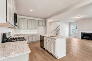 Modern Somerset Hill kitchen with white cabinets, granite counters, island sink, and open view of living room fireplace.