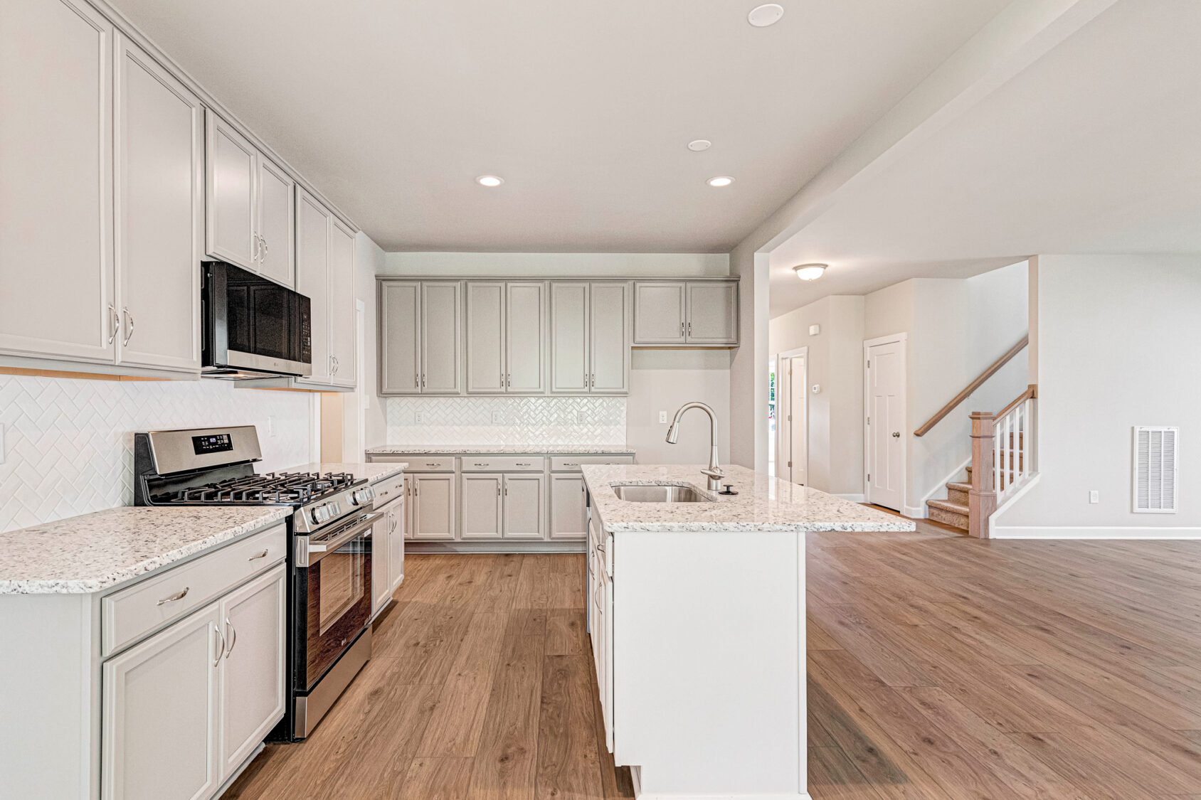 Modern Somerset Hill kitchen with white cabinets, granite counters, wood flooring, and open to living area.