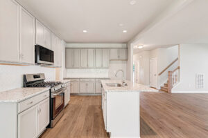 Modern Somerset Hill kitchen with white cabinets, granite counters, wood flooring, and open to living area.