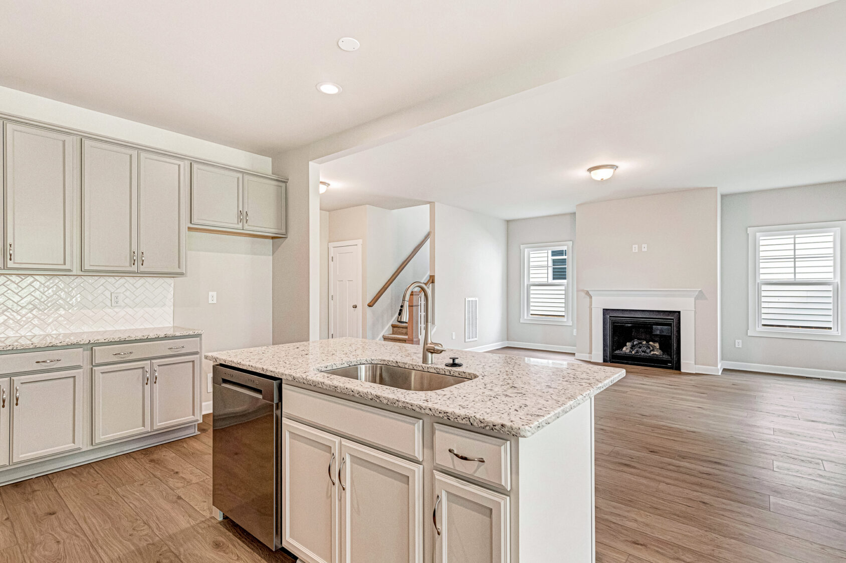 Bright Somerset Hill kitchen with white cabinets, island sink, open to living room with fireplace and wooden floors.