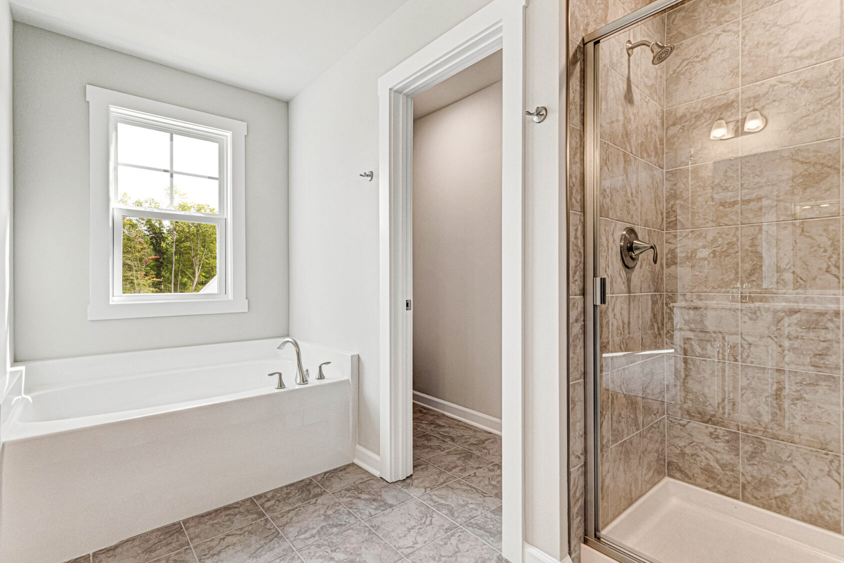 Bright Somerset Hill bathroom with soaking tub, glass shower, gray tile floor, and a window with outdoor view.