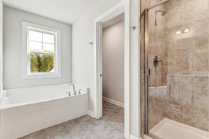 Bright Somerset Hill bathroom with soaking tub, glass shower, gray tile floor, and a window with outdoor view.