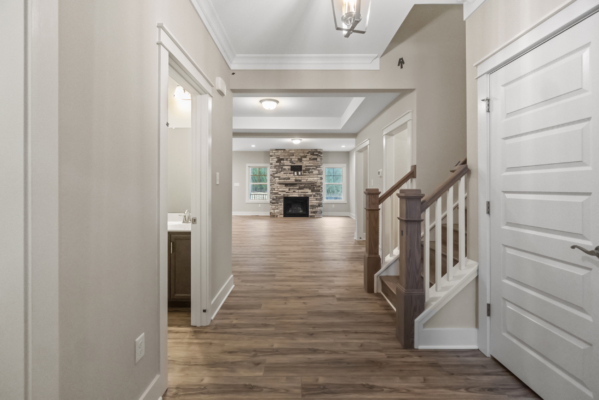 A modern hallway with hardwood floors leads to a living room featuring a stone fireplace, perfect for new homes in Virginia.