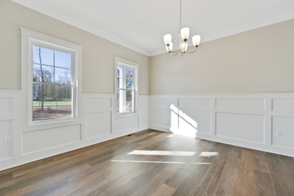 Bright empty room with wood floors, beige walls, white wainscoting, and a chandelier in a new home in Virginia.